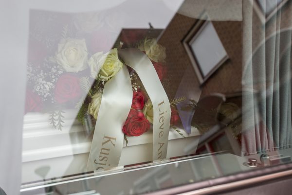 Kist in rouwauto Een kist met linten en bloemen gezien door het raam van een rouwauto, afscheidsfotografie
